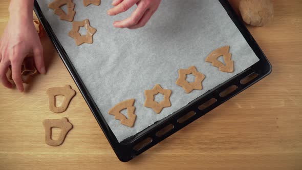 Placing various christmas gingerbread shapes on a baking tin on brown wooden table topdown video