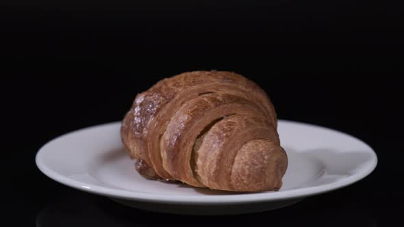 Croissant on white plate rotating in front of camera, Close-up rotates