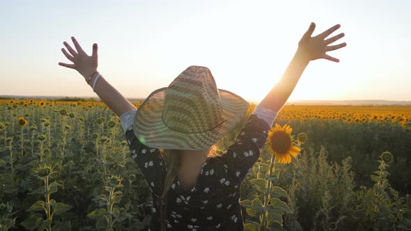 A Happy Little Girl in the Hat Is Smiling at the Field of Sunflowers at Sunset Time