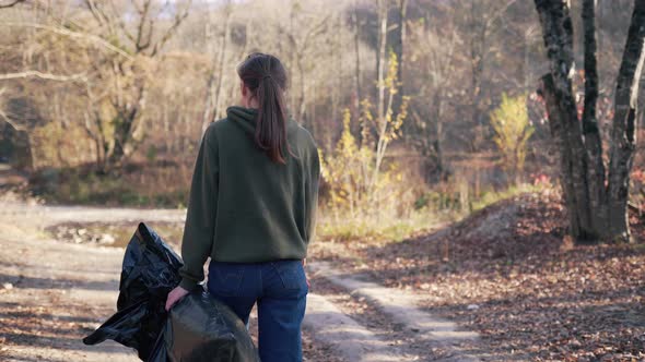 A Female Volunteer Holds a Trash Bag and Gloves in Her Hands While Collecting Garbage