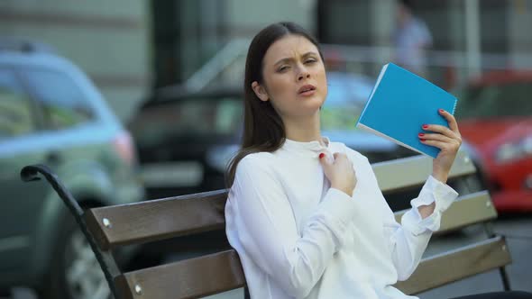 Woman on Bench Waving With Notebook Feeling Sick in Hot Weather Conditions