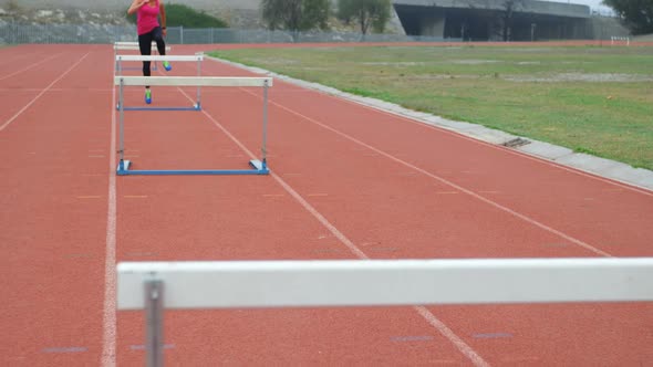 Caucasian female athlete running over hurdles on a running track at sports venue 4k