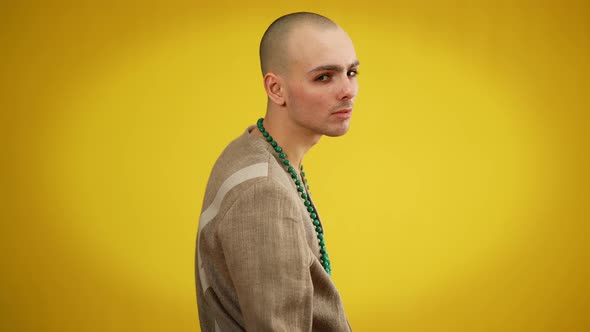 Male Queer in Women's Jacket and Green Necklace Turning to Camera Posing at Yellow Background