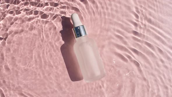 Cosmetic Bottle with Pipette on Water with Drops on a Pink Background