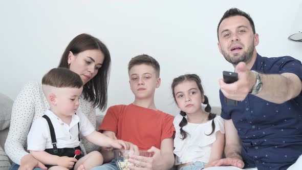 Beautiful Family Watching TV and Eating Popcorn Sitting at Home on the Couch