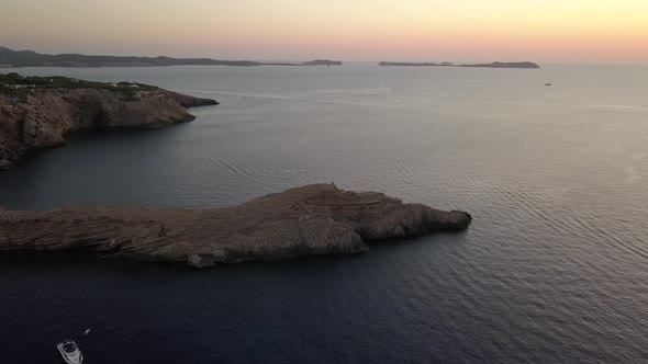 Zoom in on a small peninsula in Ibiza at goldenhour at the top four tourists. In the background the