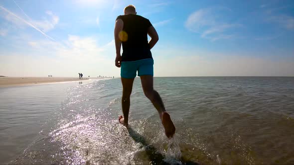 Man in shorts, running in water, on a sunny day, back shot