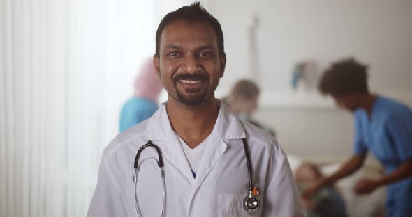 Portrait of Mature Indian Doctor Looking at Camera and Talking in Hospital Ward