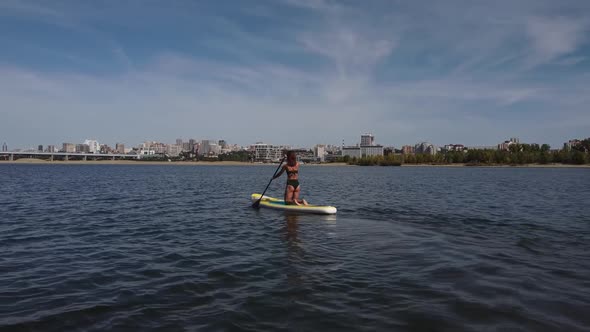 Caucasian Woman is Riding a SUP Board on the River in the City