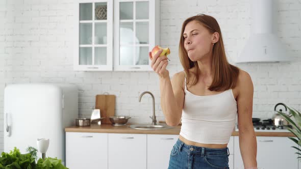 Young sports girl in white is biting a fresh red apple. Healthy food. Healthy vegan with fruits.