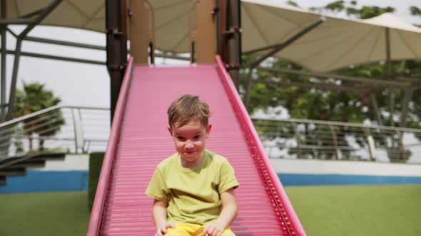 Child Laughs Happily Slides Down Children's Slide in Children's parkLittle Boy Swing in Playground