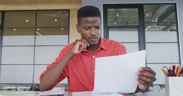 African american creative businessman at desk, reading document and talking during video call