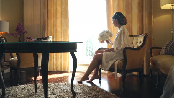 Young Bride Is Sitting By the Window in a Luxury Hotel with a Bouquet of Flowers