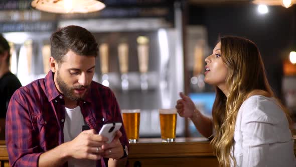 Young Couple In A Bar Arguing Over The Time He Spend On Social Media With His Smartphone