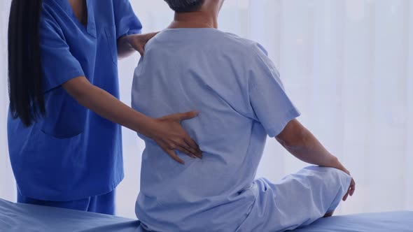Physiotherapist examining back of elderly patient on hospital bed
