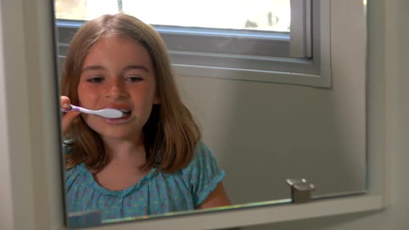 Cheerful Tanned Girl in the Blue Blouse is Brushing Her Teeth in the Bathroom