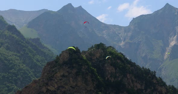 Paragliding Pilots Fly Paragliders Among Clouds and Green Mountains