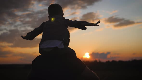 Silhouette Father and Little Son Playing on Meadow. They Rising Up Hands Imitating a Flight at