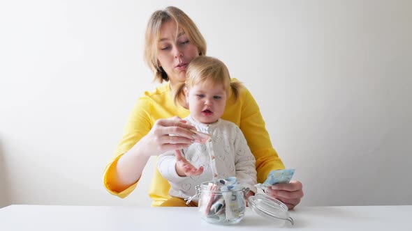 Portrait of a mother and a little child counting money and putting it in a glass jar.