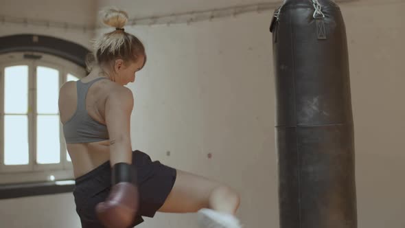 Side View of Powerful Woman Punching and Kicking Heavy Bag