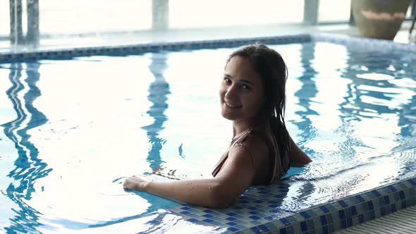 Closeup Shot of Young Woman Enjoying and Relaxing in Indoor Swimming Pool Looking at Camera and