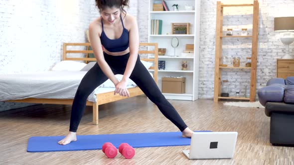 20s Young Woman in Sportswear Stretching Exercises While Watching Fitness Videos on Laptop Online