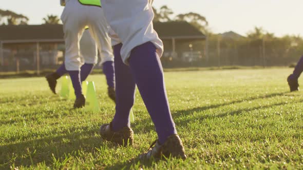 Diverse group of female baseball players exercising on pitch, running between cones