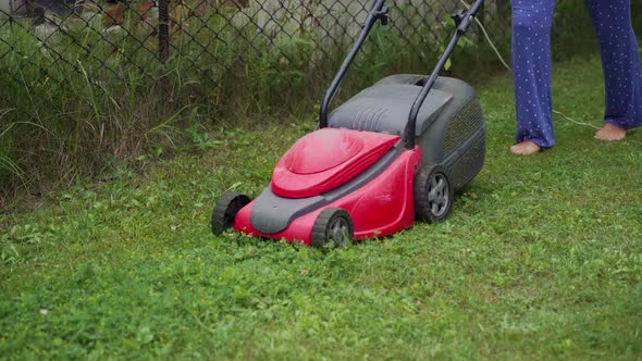 girl is mowing weeds by lawn mower in the garden near the fence in the summer