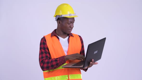 Young Happy African Man Construction Worker Thinking While Using Laptop