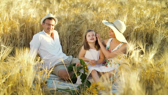 Little girl throwing sunflower petals on family picnic in wheat field