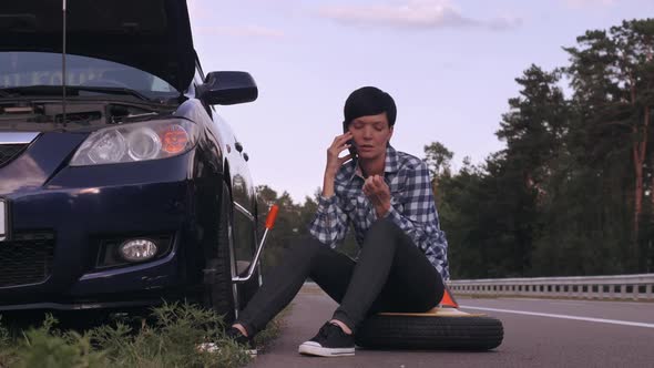 Driver Try To Change a Tire Outdoors Using Smartphone