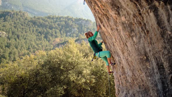 Strong and Powerful Woman Rock Climber Climbs Hard Tough Rock Route on Overhanging Cliff on
