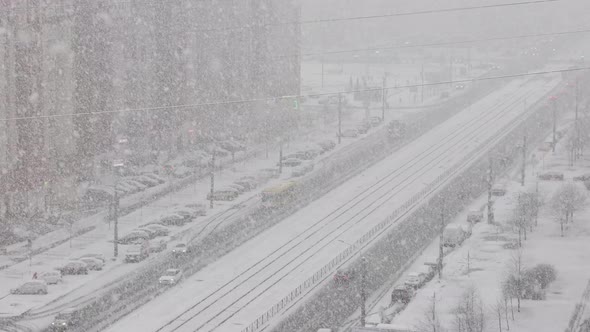 Heavy snowfall on city streets. Traffic of cars on snowy streets. View from window.