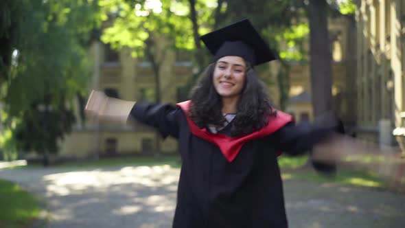 Cheerful Young Beautiful Woman in Graduation Toga Dancing at University Campus in the Morning