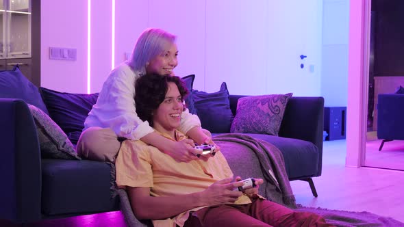 Couple at Home Playing Video Games. Girl Hug the Boy From the Back Holding Joystick in Her Hands