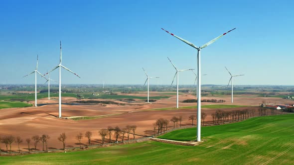 Large wind farms in the field with a small plowing tractor in sunny day