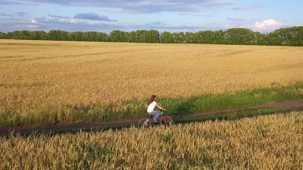 Girl with a Guy Riding a Bike Along a Wheat Field