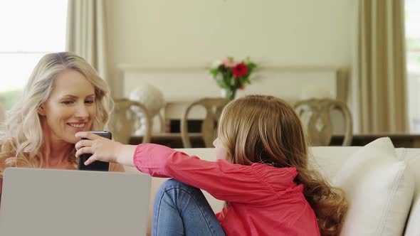 Mother and daughter using mobile phone in living room