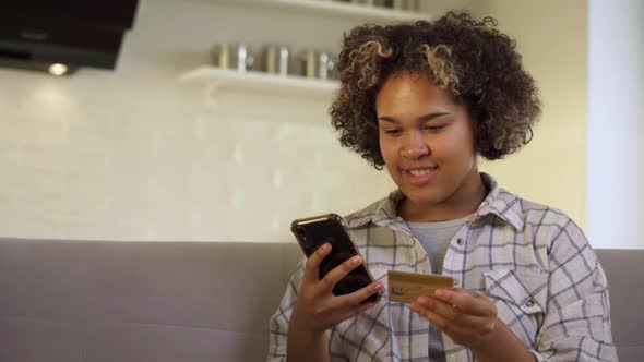 A Happy Young AfricanAmerican Woman Pays Through Her Smartphone at Home
