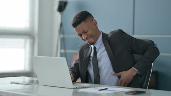 African Businessman having Back Pain while using Laptop in Office