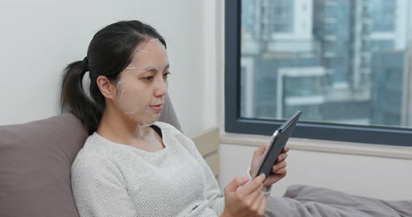 Woman study on tablet computer with apply paper mask on face at home