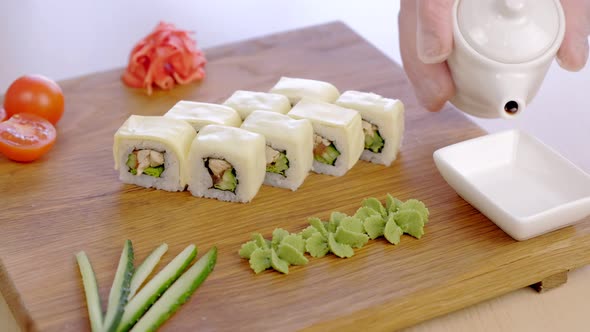 Cook Serves Rolls with Chicken Cucumber Greens and Cream Chesse on Top on Wooden Board with Wasabi