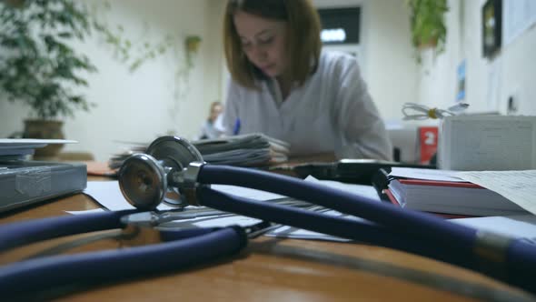 Young Nurse Working at Office Desk and Writing Medical Records Stethoscope on Foreground
