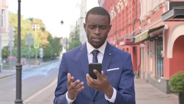 Walking African Businessman Reacting to Loss on Smartphone