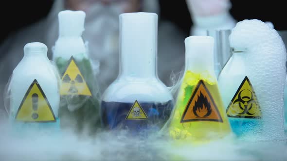 Marked Dangerous Liquids Evaporating in Flasks in Front Laboratory Worker