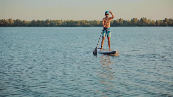 Man Floating On Sup Board At Idyllic Evening. Swimming On Stand Up Paddle Board. Surfer Water Sports