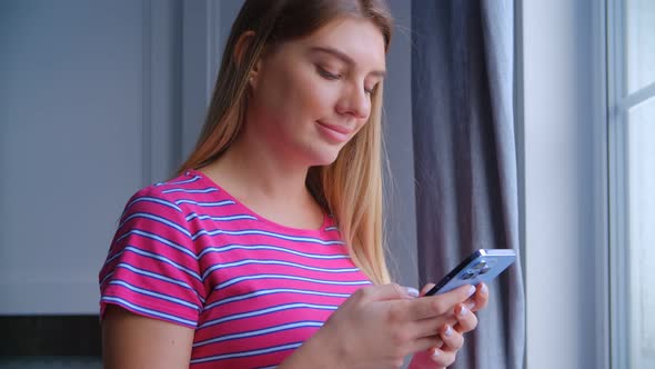 Pretty white female using modern smartphone for communication online near window in 4k video