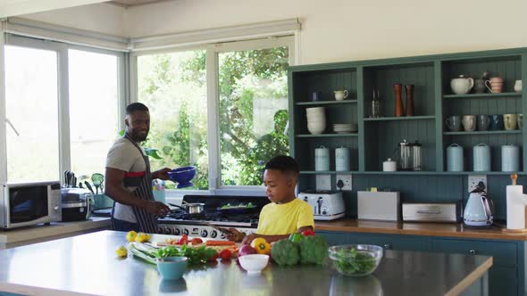 African american father and son in kitchen wearing aprons and preparing dinner together