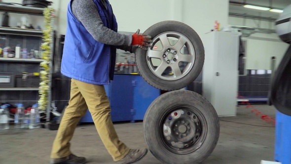 Worker rolls a two wheels in a car repair shop