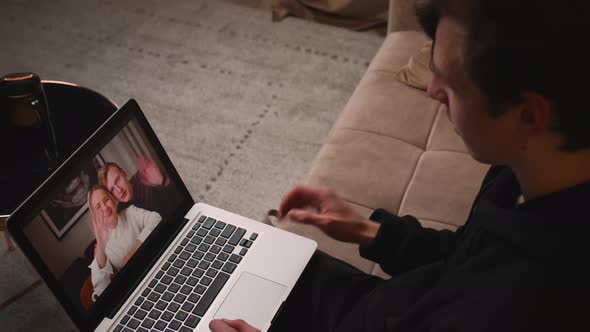 Young Man Waving Hand Has Video Calling on Laptop with Friends Sitting on Couch at Home